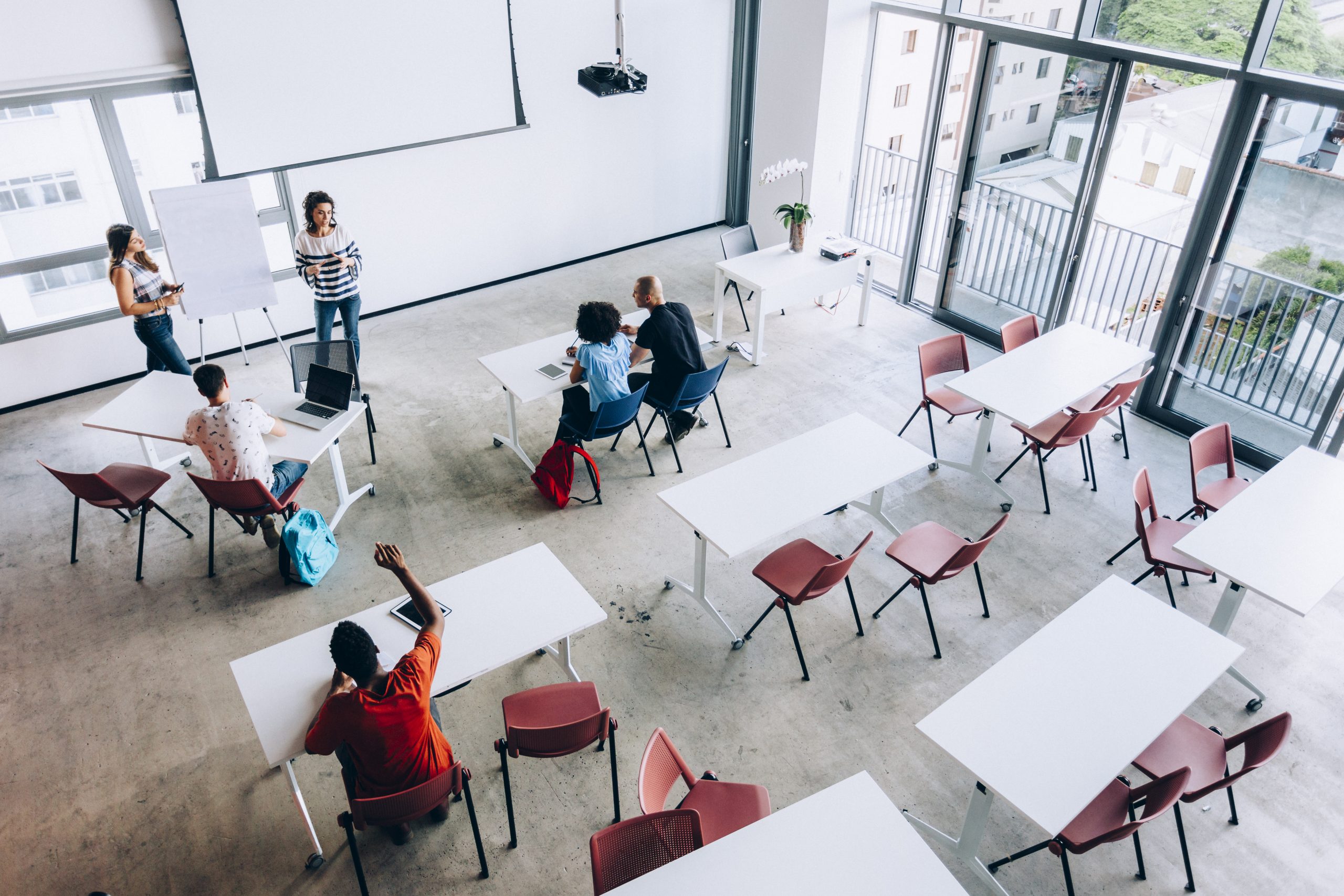 A classroom with students listening to an instructor, with one student raising their hand